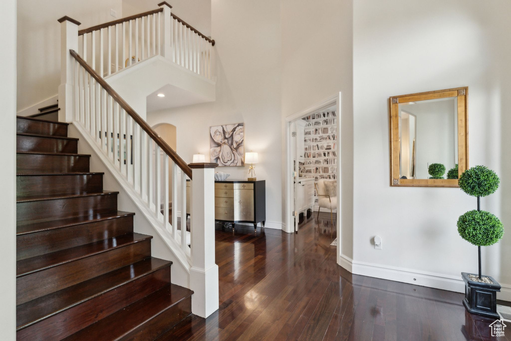 Foyer entrance with wood finished floors, a high ceiling, baseboards, stairway, and arched walkways