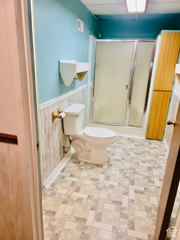 Full bathroom featuring a shower with shower door, a wainscoted wall, toilet, and wood walls