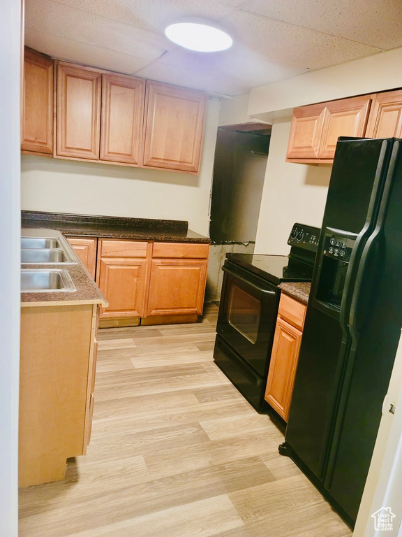 Kitchen featuring black appliances, a sink, light wood-style floors, dark countertops, and light brown cabinets