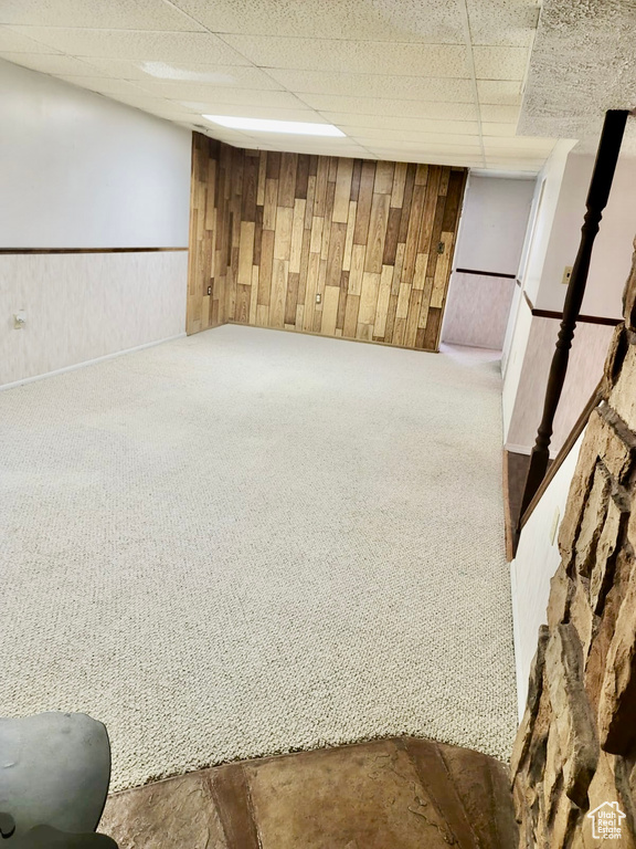 Finished basement with carpet flooring, a drop ceiling, wooden walls, and a wainscoted wall