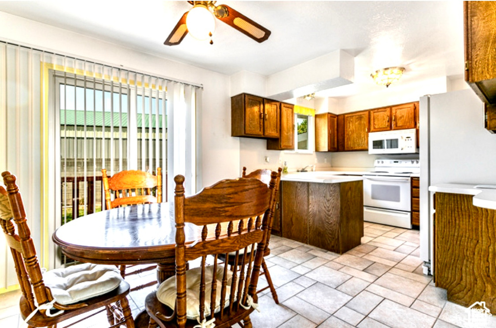 Kitchen featuring white appliances, a peninsula, a ceiling fan, light countertops, and brown cabinetry