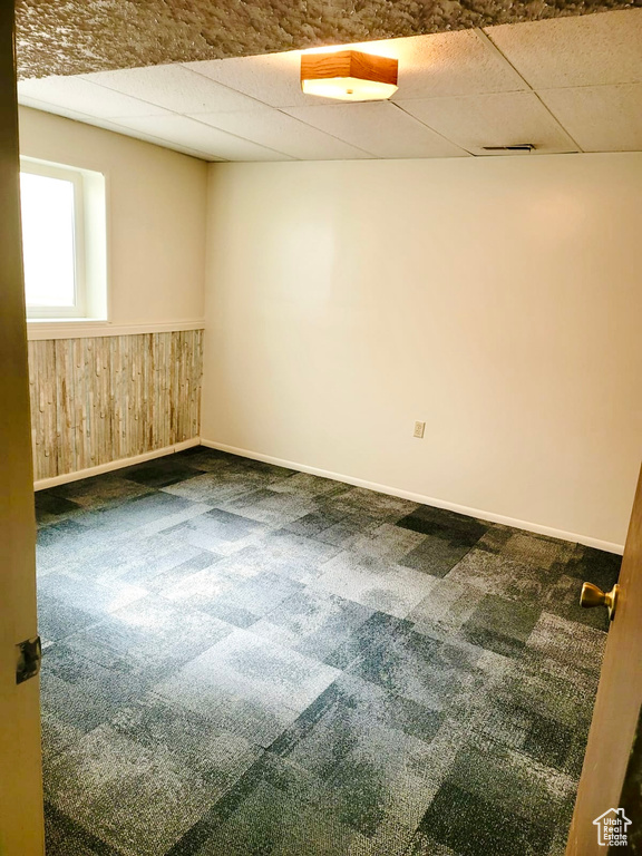Carpeted empty room with a paneled ceiling, a wainscoted wall, wood walls, and baseboards