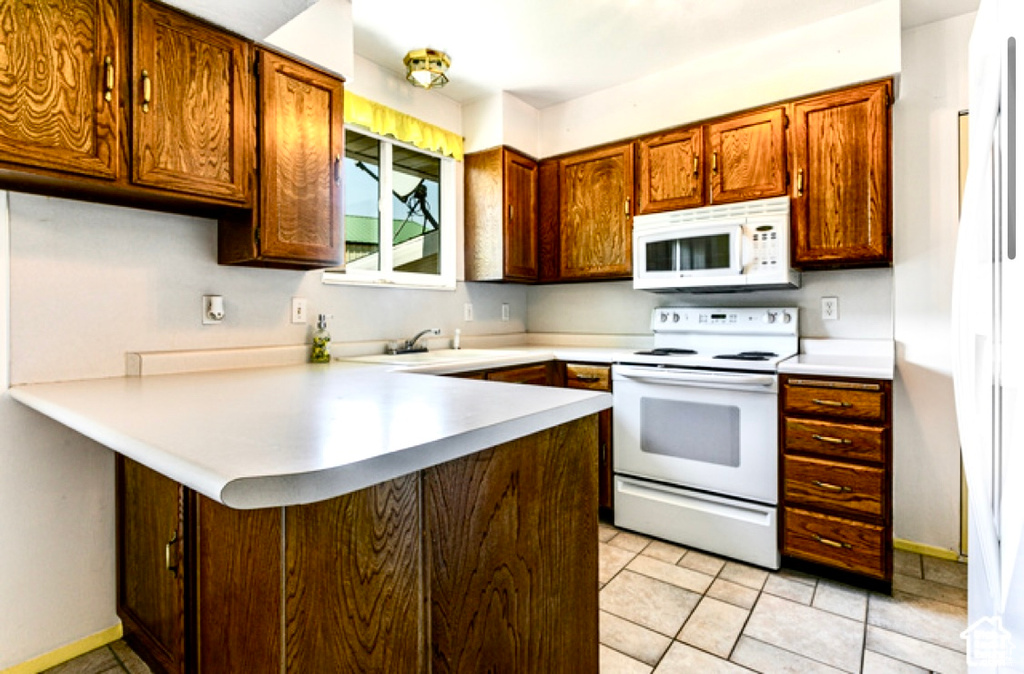 Kitchen with white appliances, a peninsula, light countertops, a sink, and baseboards