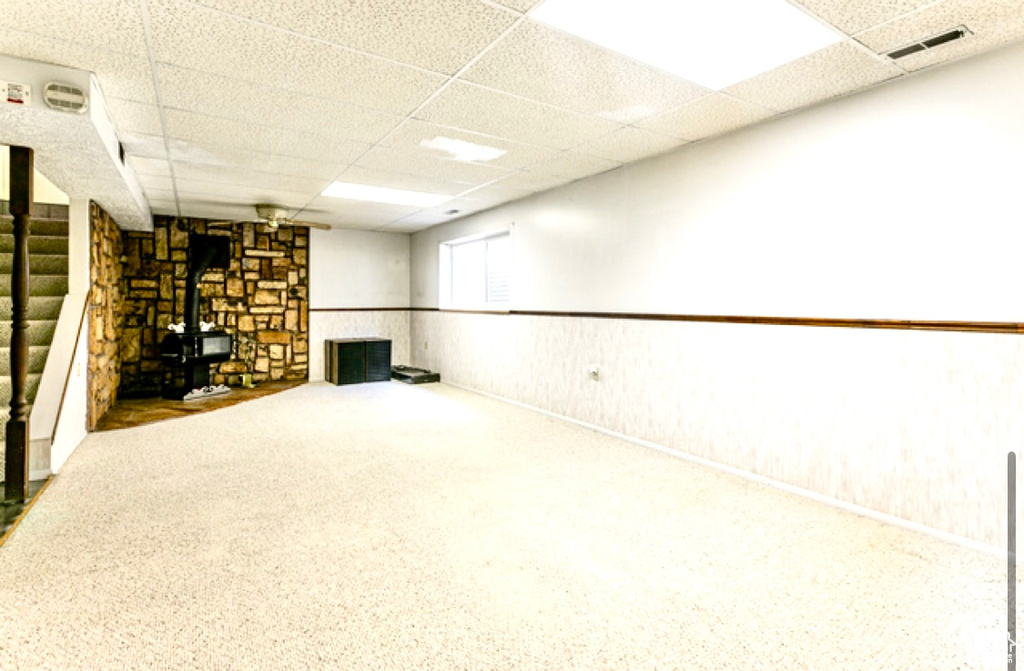 Basement featuring a wood stove, a drop ceiling, and wainscoting
