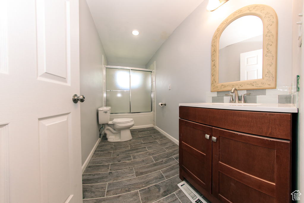 Bathroom featuring bath / shower combo with glass door, vanity, toilet, baseboards, and wood tiled floors