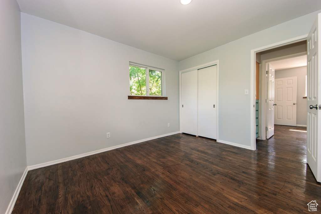 Unfurnished bedroom featuring baseboards, dark wood-style flooring, and a closet