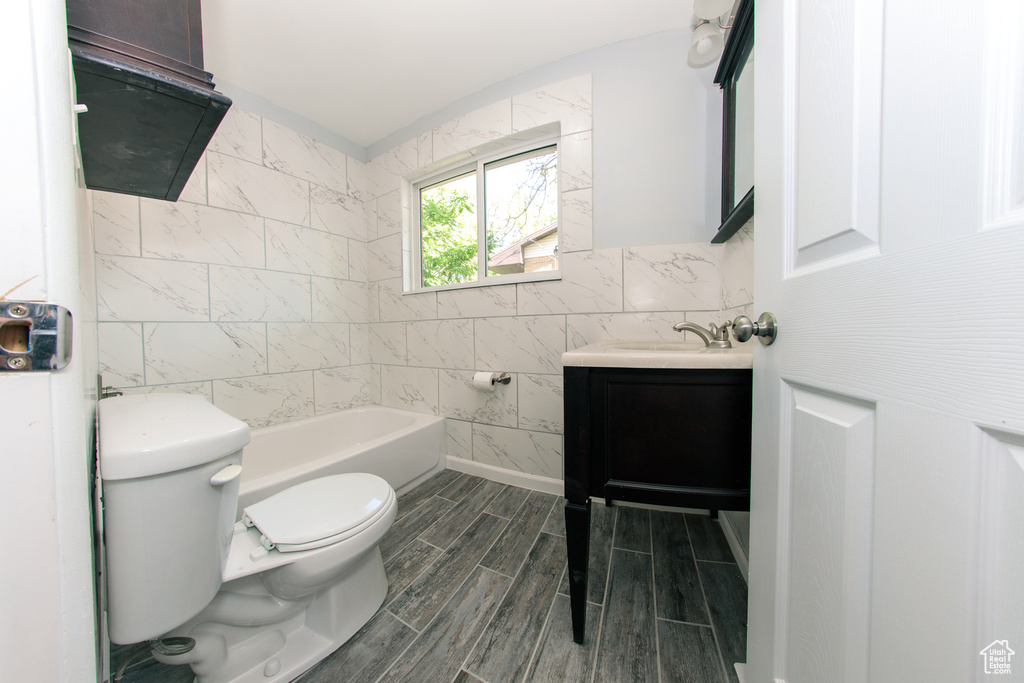 Full bath featuring tile walls, toilet, vanity, a tub to relax in, and wood finish floors