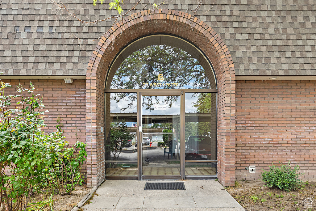 Doorway to property featuring roof with shingles and brick siding