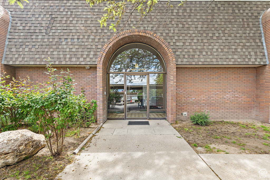 Doorway to property with a shingled roof and brick siding