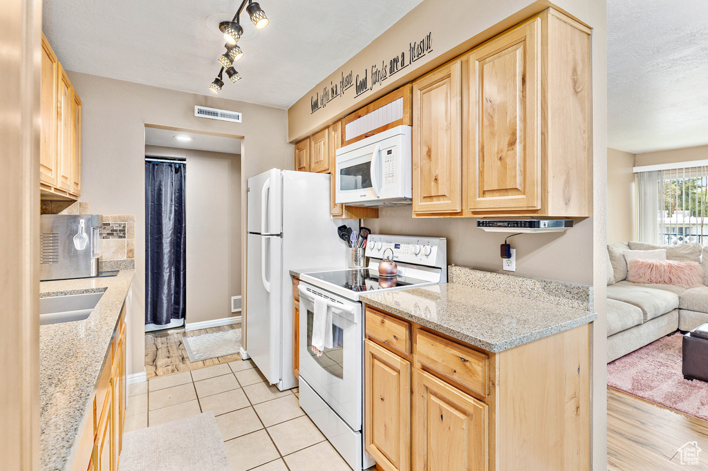 Kitchen featuring white appliances, light brown cabinets, open floor plan, and light stone countertops