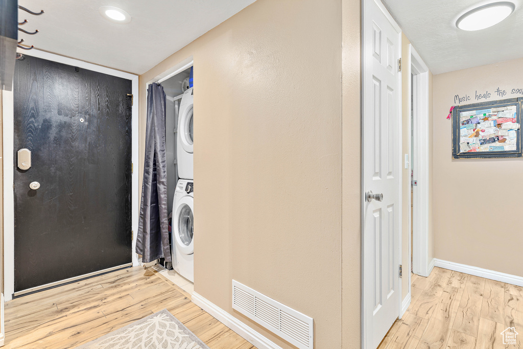 Washroom with stacked washer / drying machine, wood finished floors, and baseboards