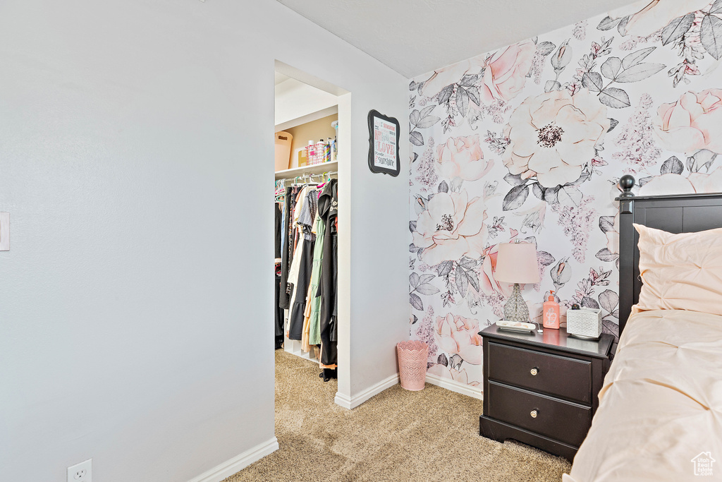 Bedroom with a spacious closet, light colored carpet, baseboards, and a closet
