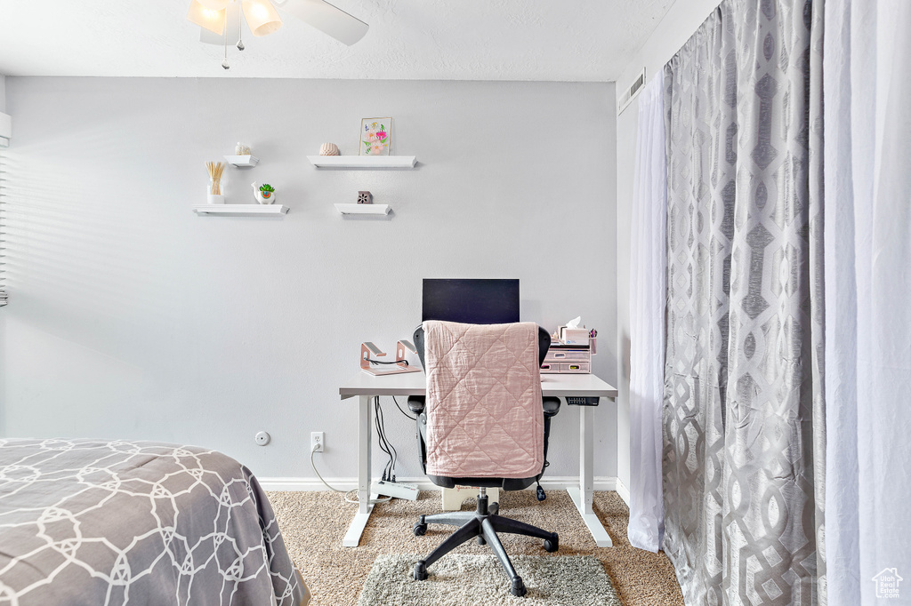 Carpeted bedroom featuring an office area, baseboards, and ceiling fan