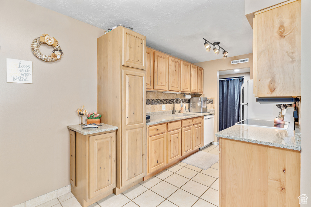 Kitchen with light brown cabinetry, white dishwasher, light tile patterned floors, backsplash, and a sink