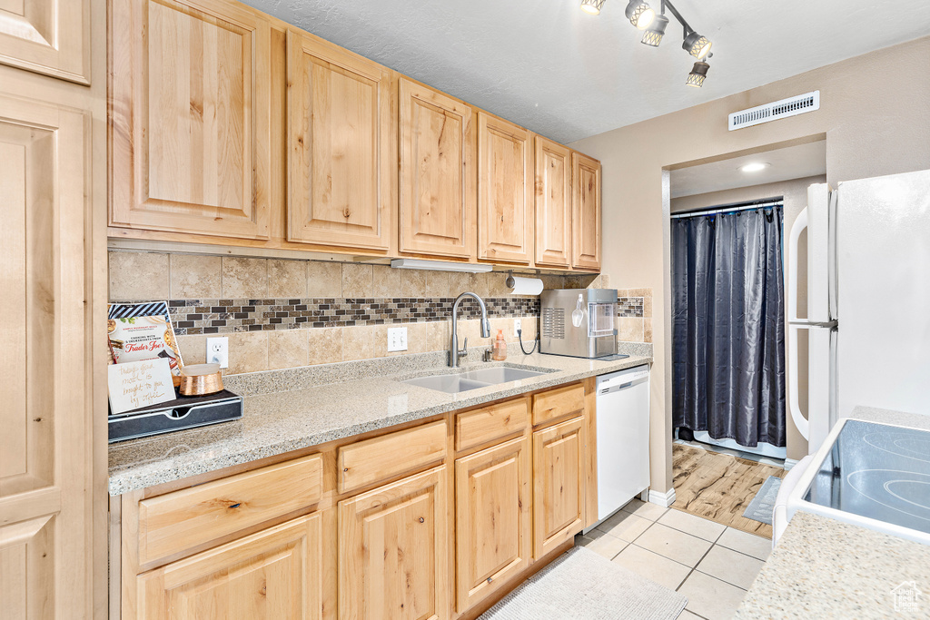 Kitchen with light brown cabinetry, a sink, white appliances, light tile patterned flooring, and backsplash