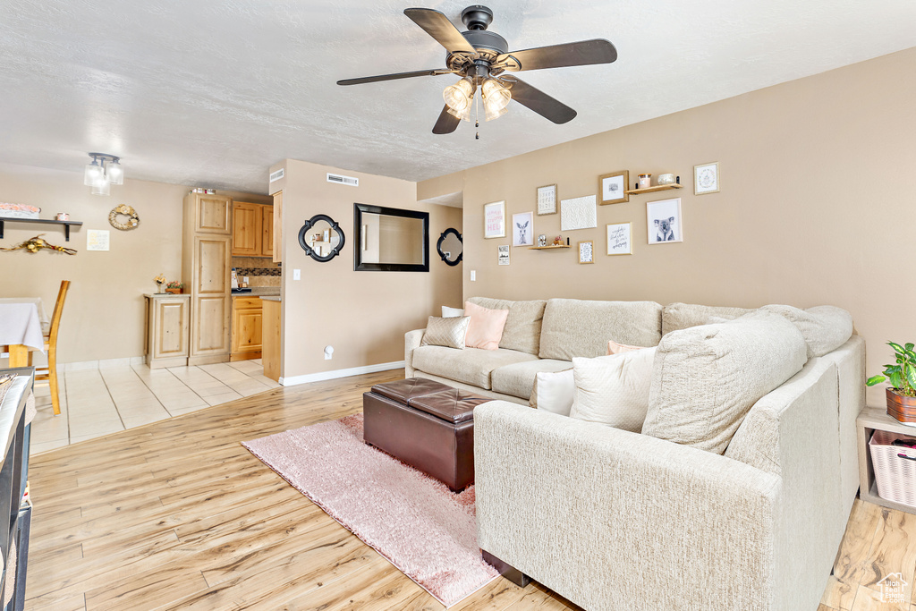 Living area with light wood finished floors, a ceiling fan, and baseboards