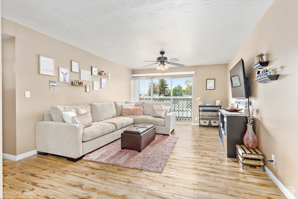 Living area featuring light wood-style flooring, a ceiling fan, baseboards, and a textured ceiling