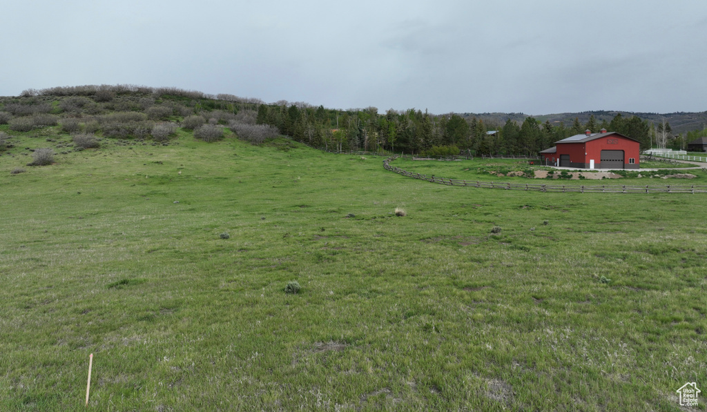 View of grassy yard featuring a rural view, an outdoor structure, a garage, and a pole building