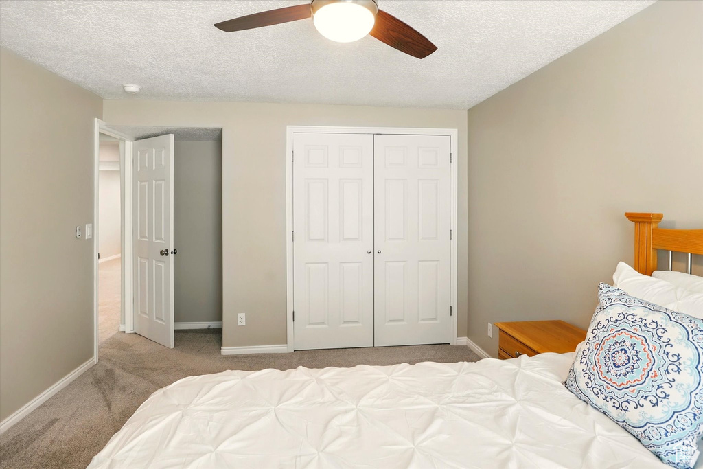 Carpeted bedroom featuring a closet, a textured ceiling, baseboards, and ceiling fan