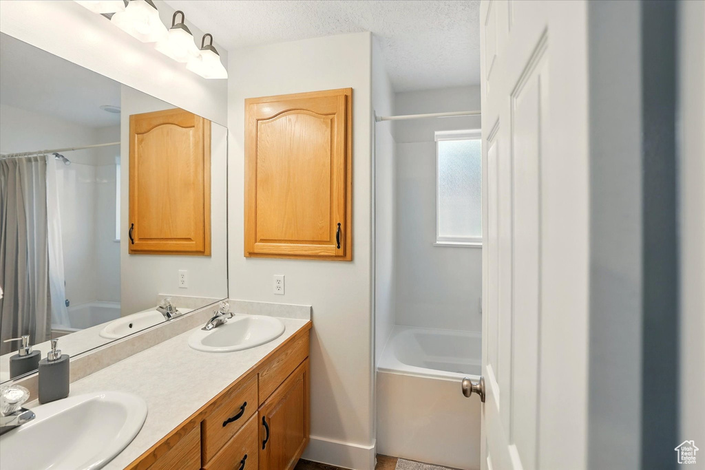 Full bath with shower / tub combo, double vanity, and a textured ceiling