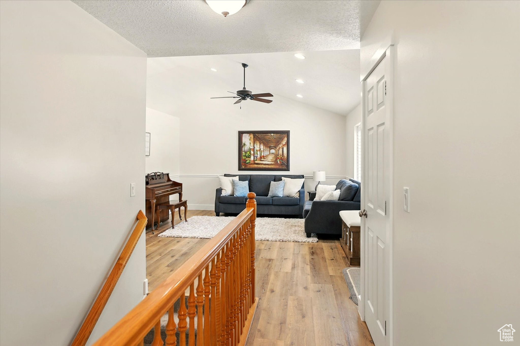 Hall featuring light wood-style floors, vaulted ceiling, a textured ceiling, and baseboards