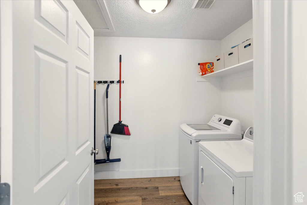 Clothes washing area featuring washing machine and clothes dryer, wood finished floors, baseboards, and a textured ceiling