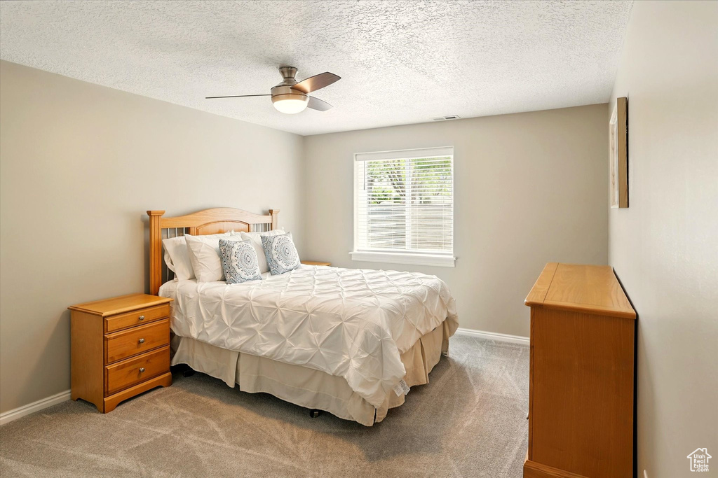Carpeted bedroom with a textured ceiling, baseboards, and a ceiling fan