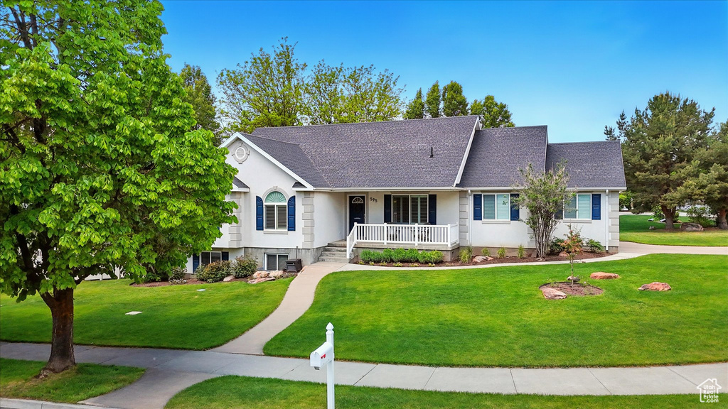 View of front of home with covered porch, roof with shingles, and a front lawn