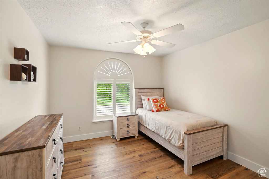 Bedroom with baseboards, wood finished floors, a textured ceiling, and a ceiling fan