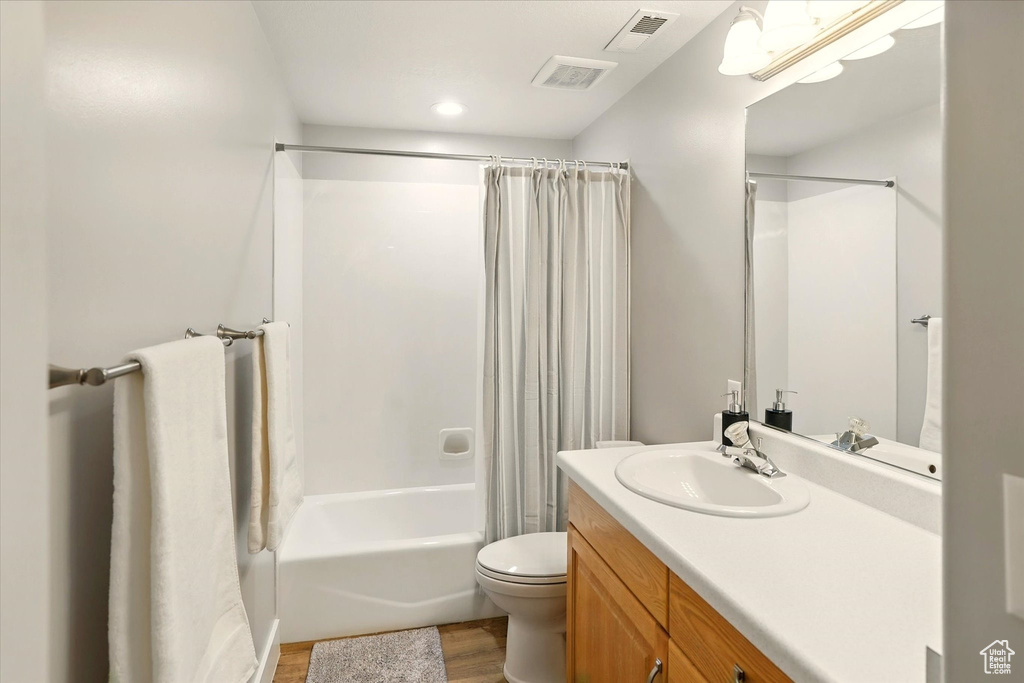 Bathroom with wood finished floors, toilet, vanity, and shower / tub combo with curtain