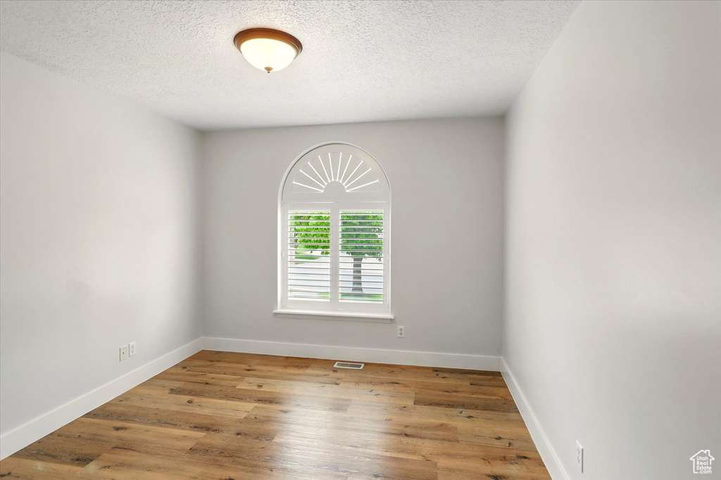 Unfurnished room featuring a textured ceiling, baseboards, and wood finished floors