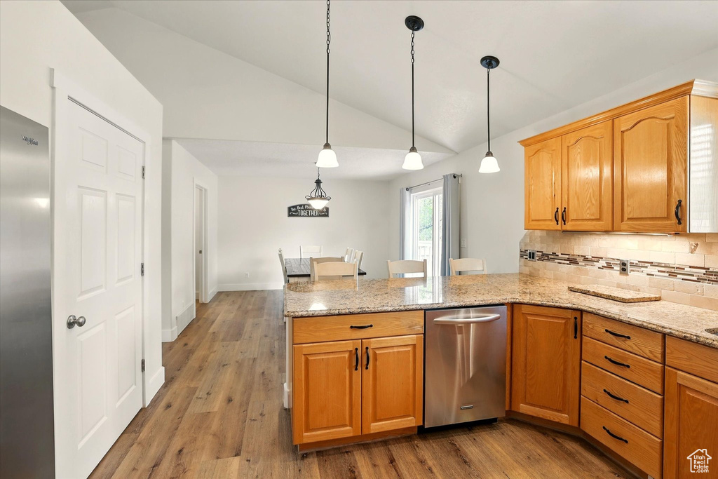 Kitchen featuring a peninsula, vaulted ceiling, stainless steel appliances, tasteful backsplash, and light stone countertops