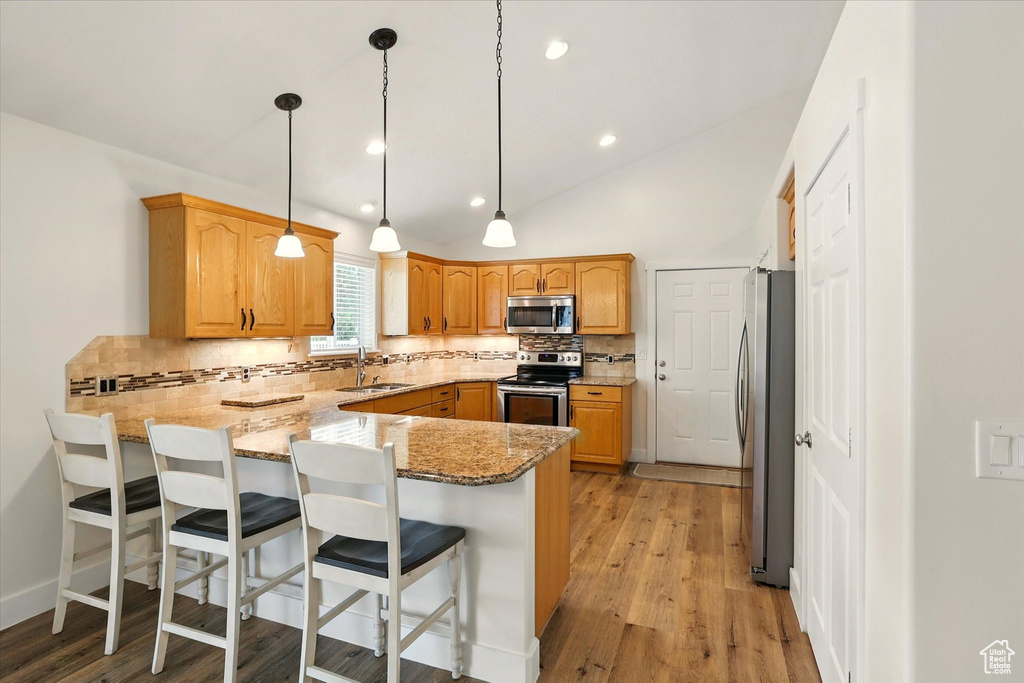 Kitchen featuring appliances with stainless steel finishes, a peninsula, a sink, backsplash, and light stone counters