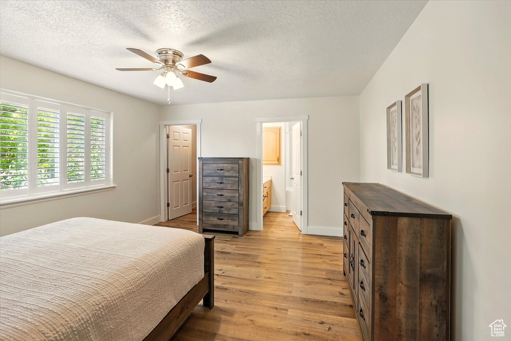 Bedroom featuring light wood-style flooring, baseboards, ensuite bath, a ceiling fan, and a textured ceiling