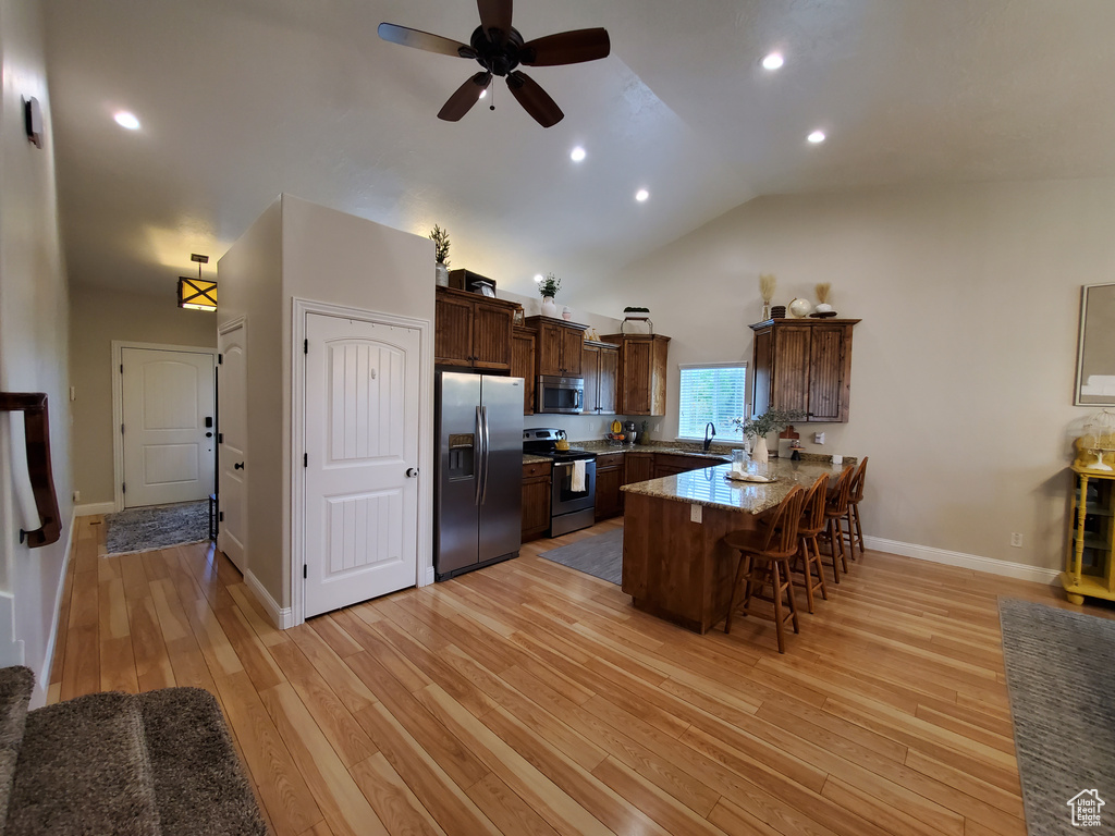 Kitchen with appliances with stainless steel finishes, a peninsula, a breakfast bar area, light wood-style flooring, and a ceiling fan
