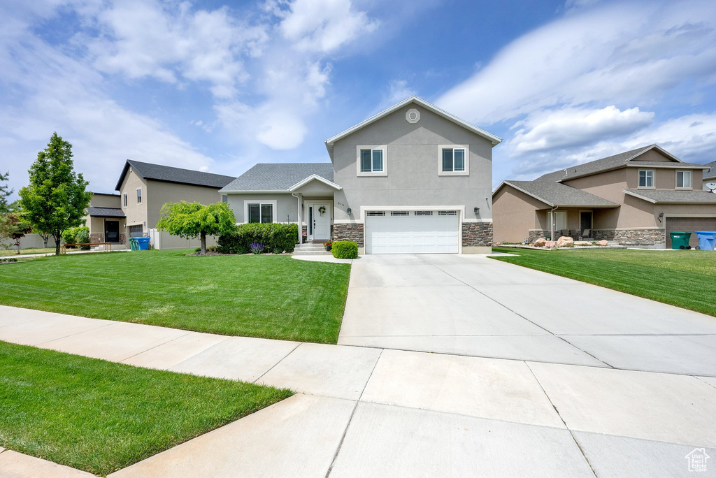 View of front of property with a garage, stone siding, stucco siding, concrete driveway, and a front lawn