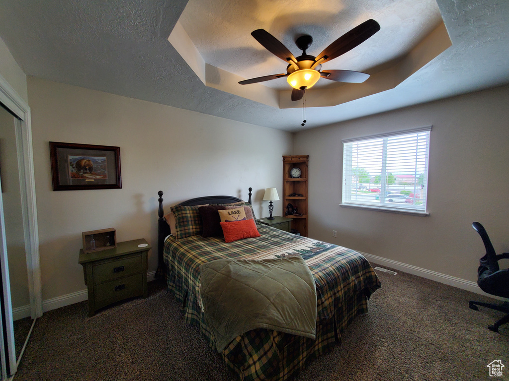 Bedroom with dark carpet, baseboards, a raised ceiling, and ceiling fan