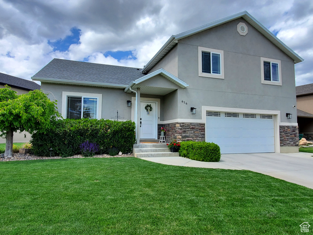 View of front of home with stucco siding, a garage, concrete driveway, stone siding, and a front lawn