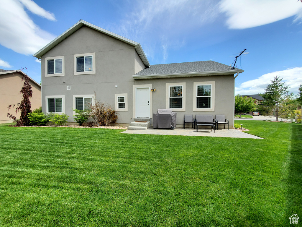 Back of house with a lawn, stucco siding, a patio area, and roof with shingles