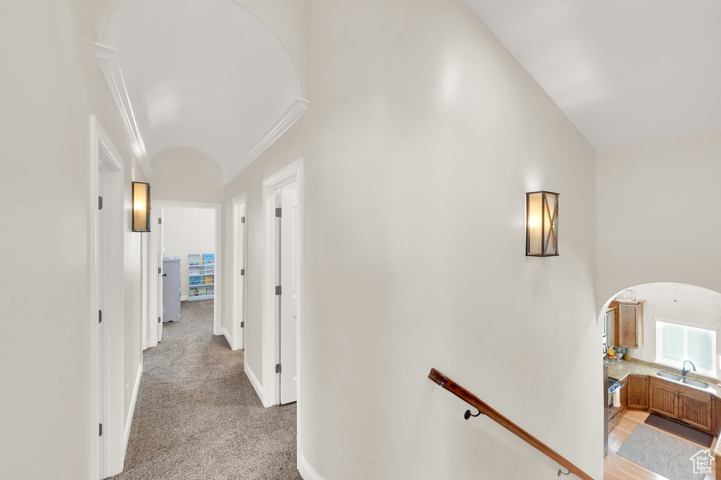 Corridor featuring arched walkways, ornamental molding, lofted ceiling, a sink, and light colored carpet