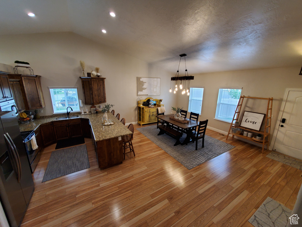 Kitchen featuring a peninsula, a kitchen bar, light wood-type flooring, a sink, and vaulted ceiling