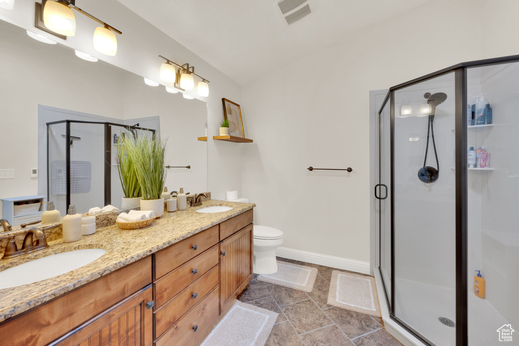 Full bathroom featuring a shower stall, double vanity, and toilet