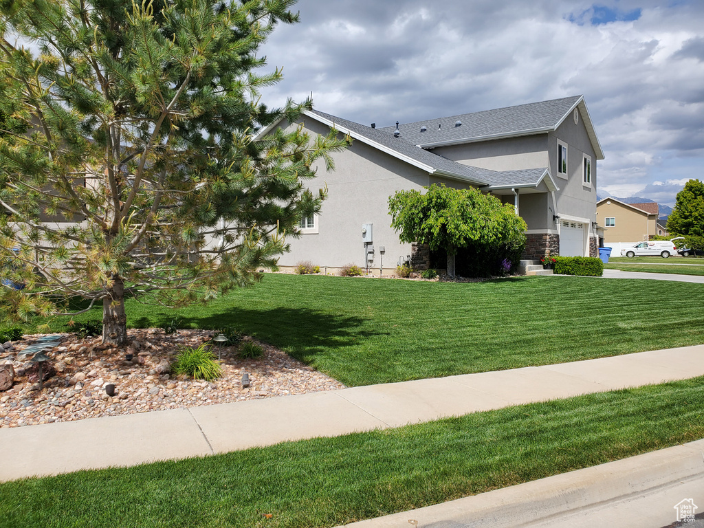 View of side of property featuring a garage, stucco siding, a yard, and stone siding