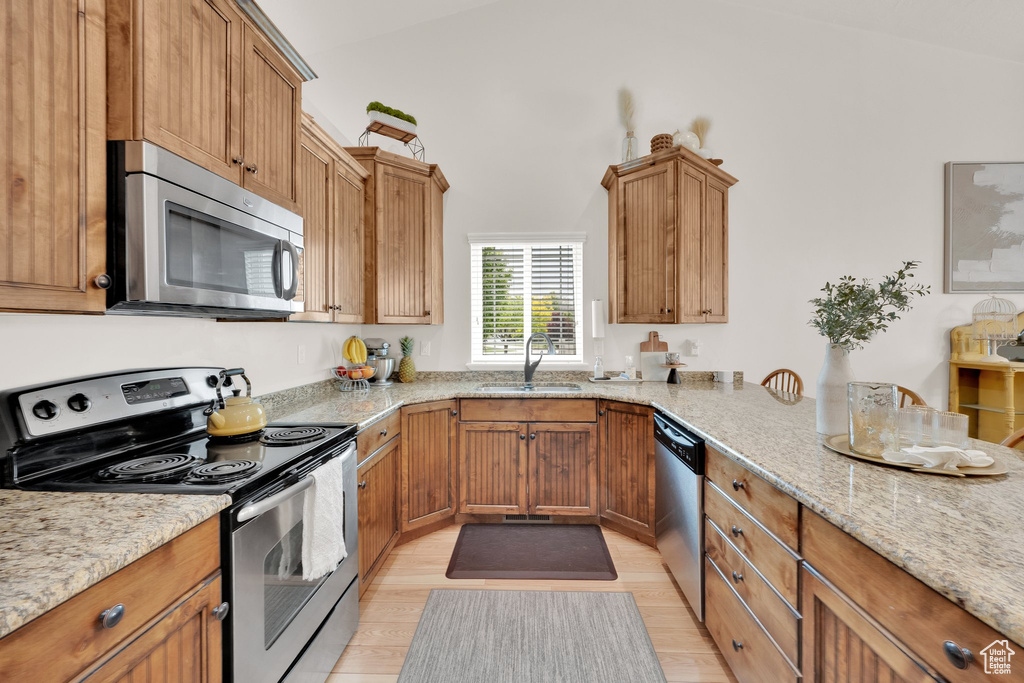 Kitchen featuring stainless steel appliances, a sink, light stone countertops, light wood-style floors, and brown cabinets
