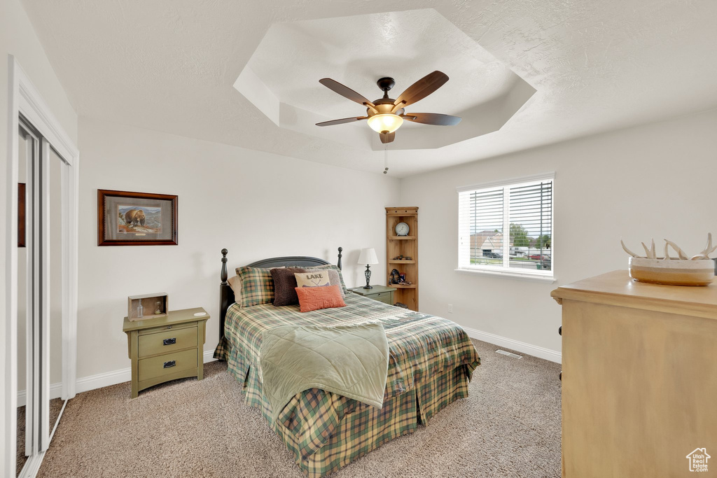 Carpeted bedroom featuring baseboards, a raised ceiling, and ceiling fan