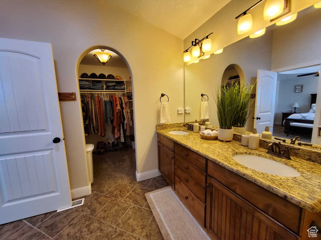 Ensuite bathroom featuring double vanity, lofted ceiling, a walk in closet, baseboards, and tile patterned floors