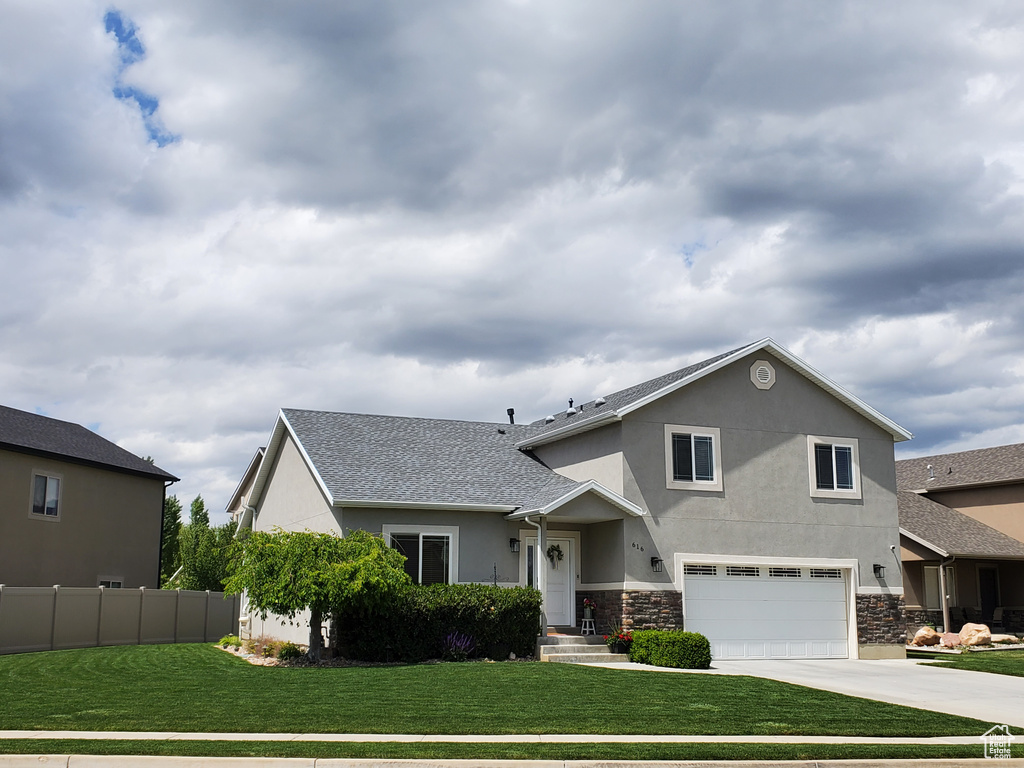 View of front facade with stucco siding, an attached garage, concrete driveway, stone siding, and roof with shingles