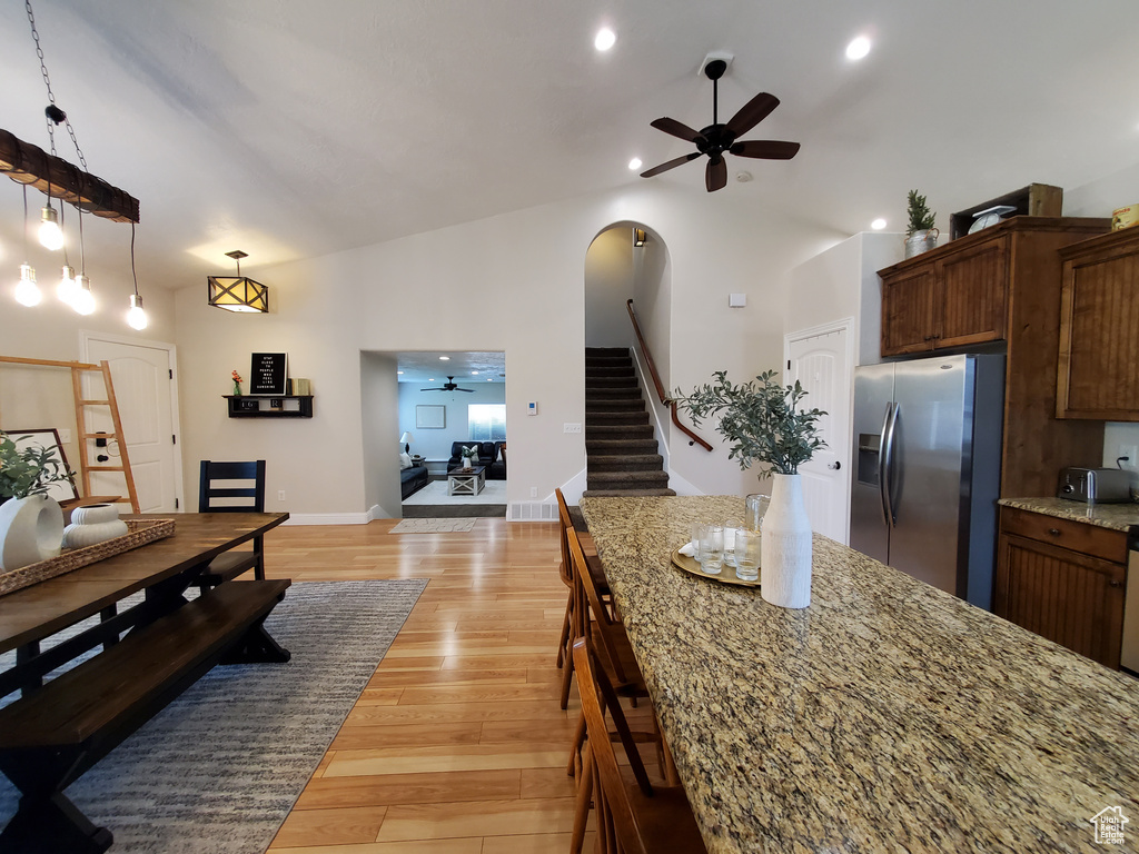 Dining space with a ceiling fan, stairs, lofted ceiling, light wood-type flooring, and arched walkways