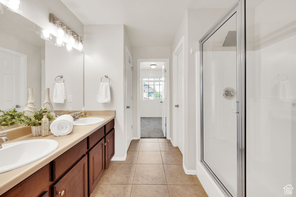 Full bath featuring a shower stall, tile patterned flooring, baseboards, and double vanity