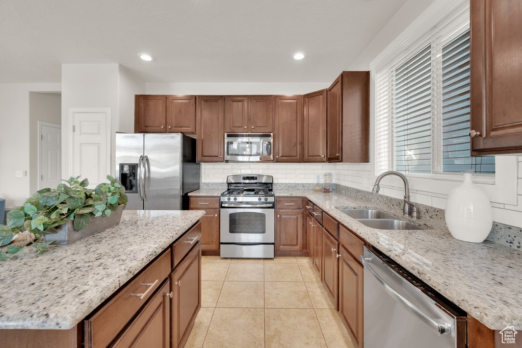 Kitchen with appliances with stainless steel finishes, a sink, tasteful backsplash, a center island, and light stone counters